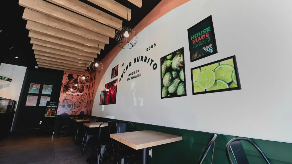 Dining tables and upholstered benches beneath wall artwork and timber ceiling slats — MUCHO BURRITO — SURREY, BC