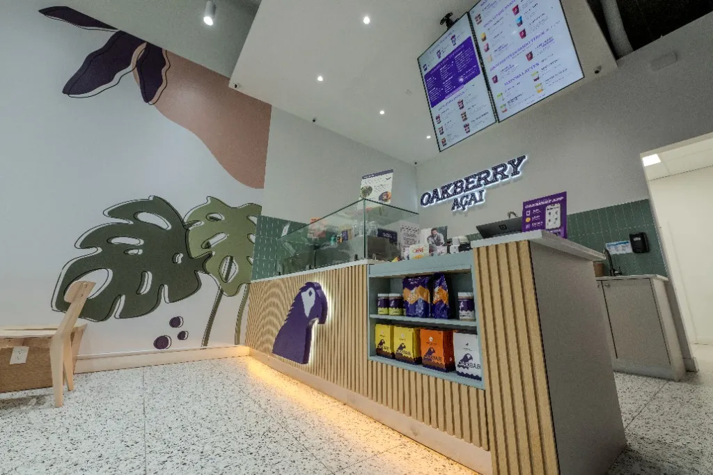 Fluted timber service counter beside a botanical mural and glass display — OAKBERRY AÇAÍ — SURREY, BC
