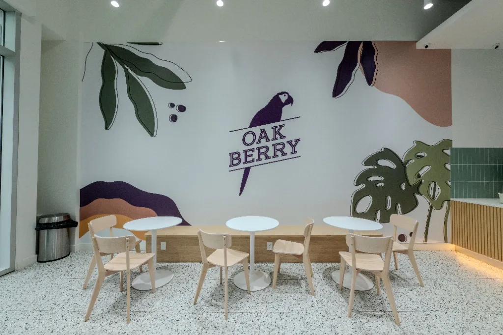 Curved bench seating and round tables beneath a botanical wall mural — OAKBERRY AÇAÍ — SURREY, BC